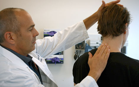 A provider consulting on a patient's back pain by touching the patient's back by his neck