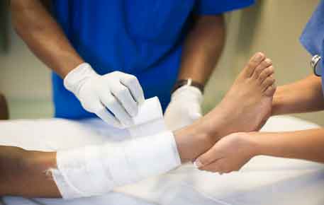 Health care providers dressing a leg wound with gauze.